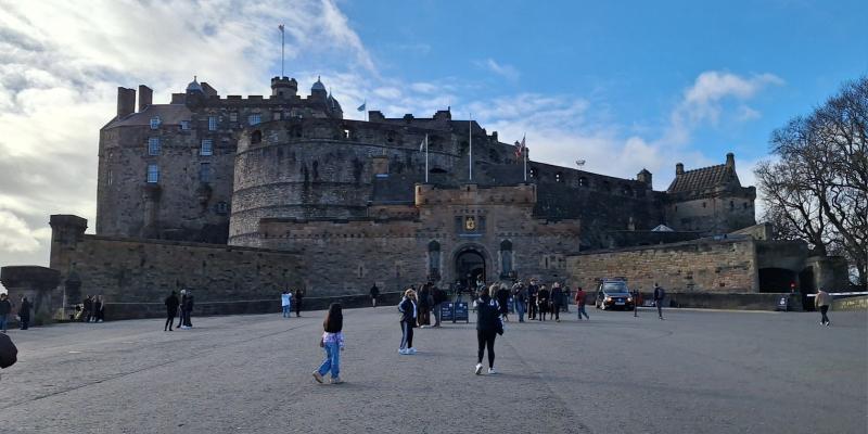 Kuvassa näkyy Edinburghin linna poutaisena päivänä. Pihamaalla on muutamia ihmisiä. Edinburghin linna on korkealle kalliolle rakennettu linna Edinburghin keskustassa. 